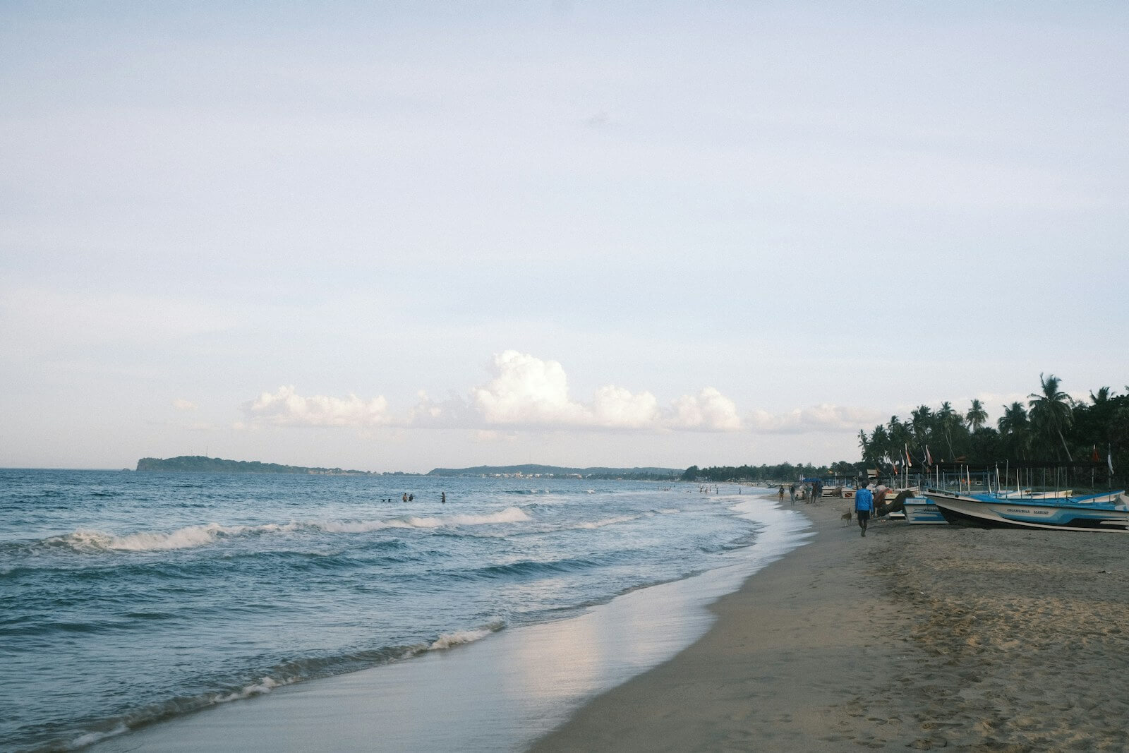 Beachgoers, boats and palm trees along the shore in Trincomalee, Sri Lanka