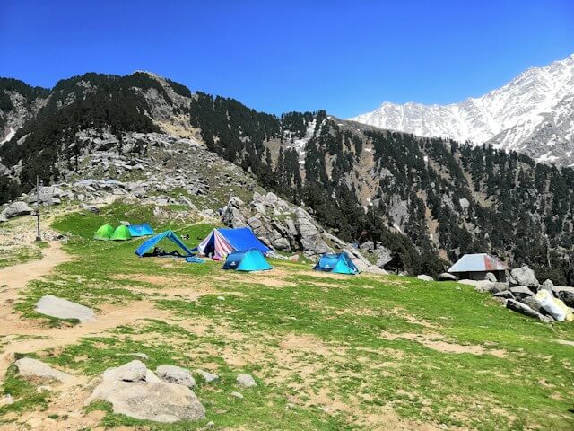 Tents on a grassy camping area beneath the Dhauladhar mountains at Triund